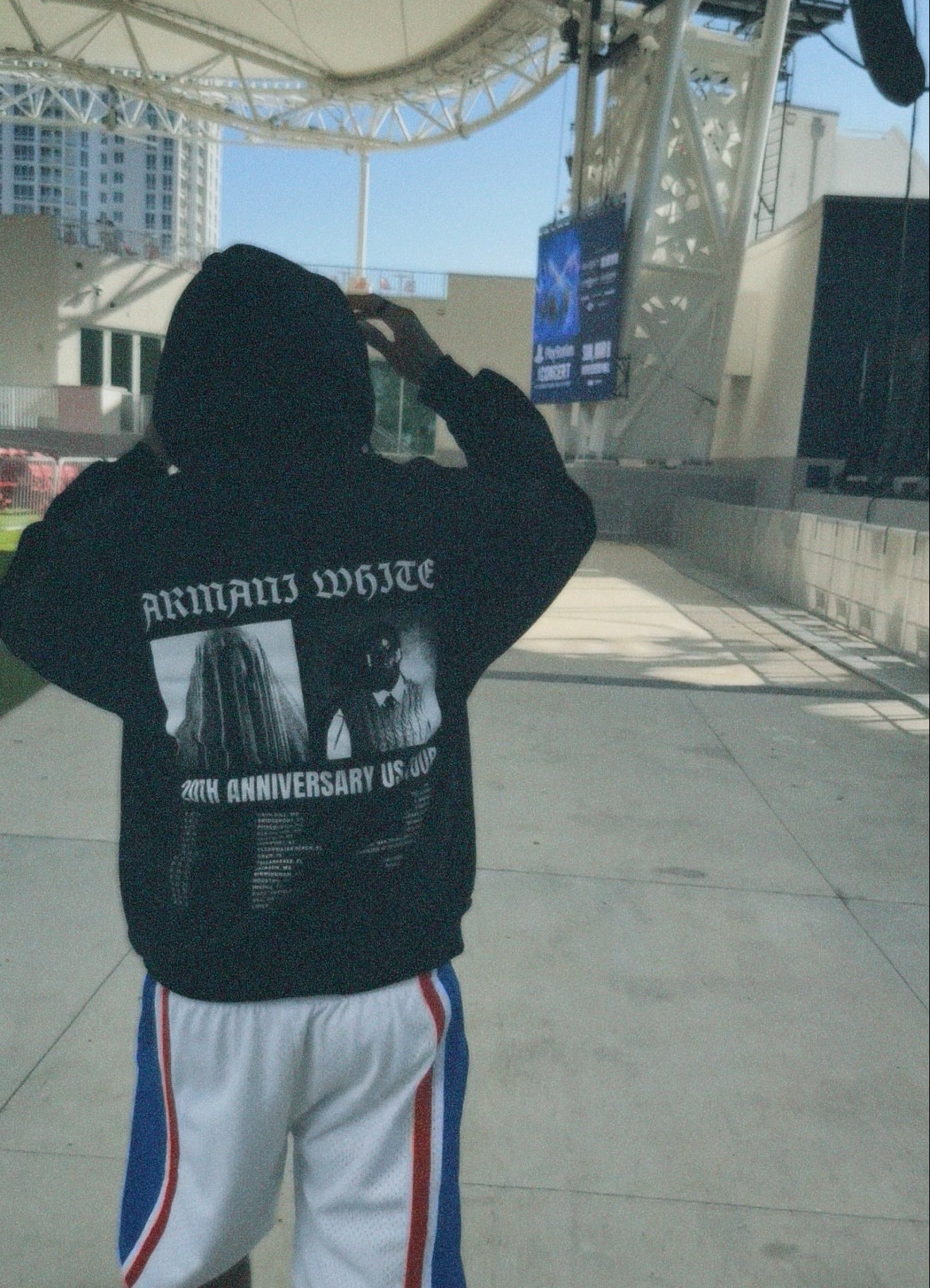 Person wearing a black hoodie with text and graphics, standing in an outdoor area.